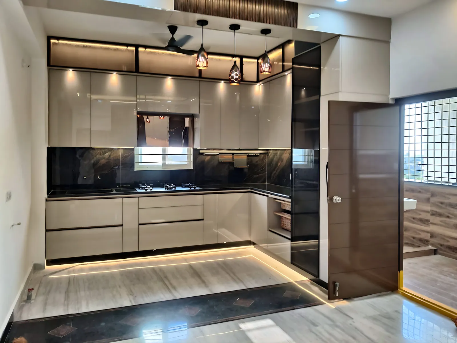 Glossy L-shaped modular kitchen with backlit glass lofts and pendant lights